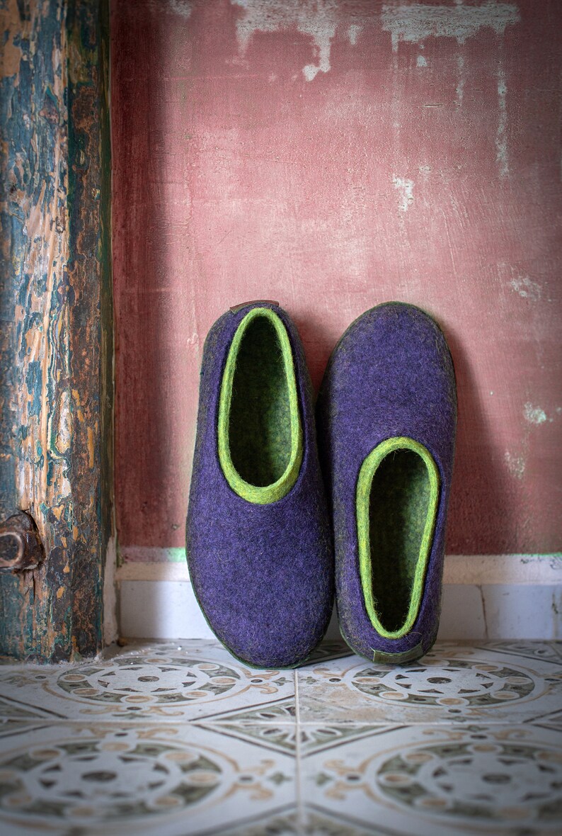 K&ouml;nnte beinhalten: Ein Paar violette Hausschuhe aus Filz mit gr&uuml;nem Filz-Futter. Die Hausschuhe stehen auf einem Fliesenboden.