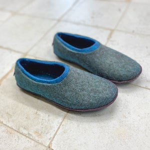 K&ouml;nnte beinhalten: Ein Paar graue Filzpantoffeln mit blauem Besatz. Die Pantoffeln haben eine abgerundete Spitze und eine flache Sohle.