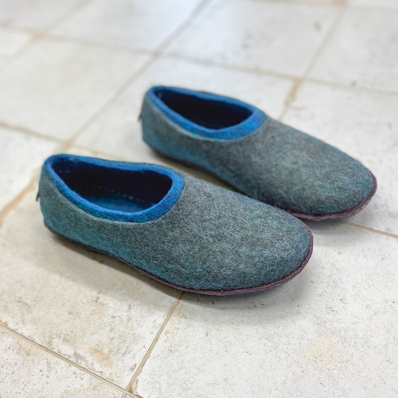 K&ouml;nnte beinhalten: Ein Paar graue Filzpantoffeln mit blauem Besatz. Die Pantoffeln haben eine abgerundete Spitze und eine flache Sohle.