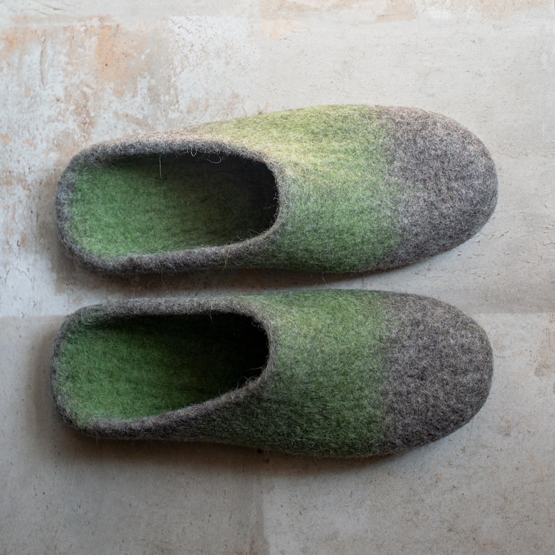 May include: A pair of green and gray felt slippers. The slippers have a rounded toe and a low-cut opening for the foot. The color gradient transitions from green to gray. The slippers are made of a soft, textured material.