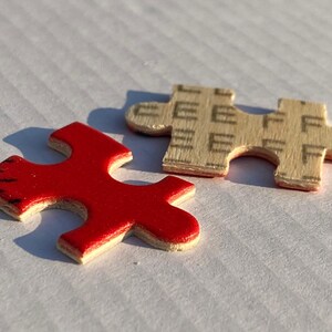 May include: Two puzzle pieces, one red and one beige, fit together to complete a larger image. The red piece has a smooth surface, while the beige piece has a textured surface.