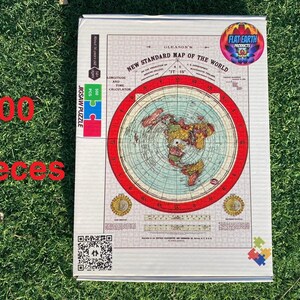May include: A 500-piece jigsaw puzzle featuring a flat earth map with a red border. The puzzle box is white with a blue and green logo that says "Flat Earth Products".
