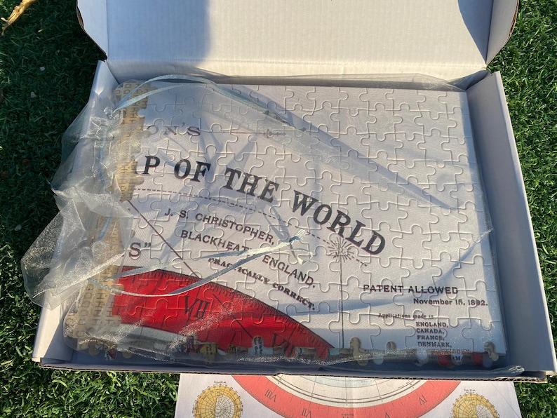 May include: A white jigsaw puzzle in a box with a blue and white ribbon. The puzzle is of a map of the world with the text "P of the World" and "Patent Allowed November 15, 1992".