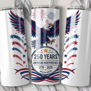 May include: White tumbler with a patriotic design. Features a stylized American bald eagle with red, white, and blue wings, and a banner that reads "250 YEARS AMERICAN INDEPENDENCE 1776-2026". Includes red and blue star and stripe accents.