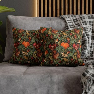 May include: Two square throw pillows featuring a dark green background with a repeating pattern of orange pumpkins, red pomegranates, brown squirrels, small birds, and moths nestled among green leaves and red berries on a dark surface.