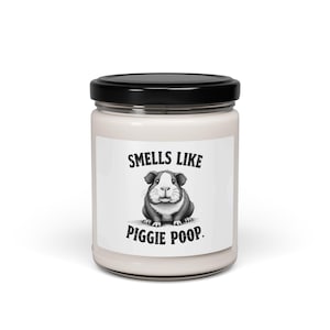 May include: A white candle jar with a black lid. The label features a black and white illustration of a guinea pig and the text "Smells Like Piggies Poop."