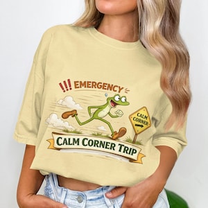 May include: A pale yellow t-shirt with a cartoon frog running towards a "Calm Corner" sign. The shirt has the words "!!! EMERGENCY" above the frog and "CALM CORNER TRIP" on a banner below.