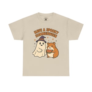 May include: Beige t-shirt with a cartoon graphic. The graphic features a friendly ghost wearing a witch hat and a hamster holding watermelon, with the text "Have a Spooky Summerween".
