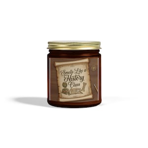 Könnte beinhalten: Ein braunes Glas mit goldenem Deckel. Das Etikett zeigt ein Schriftrollen-Design mit dem Text "Smells Like a History Class" und Illustrationen eines Globus, von Büchern und einem Kompass. Das Glas ist wahrscheinlich eine Duftkerze.