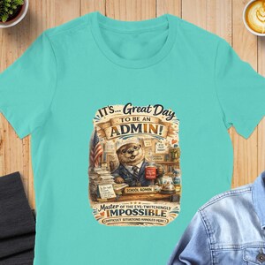 Può includere: Una t-shirt turchese a maniche corte con la grafica di una lontra in giacca e cravatta seduta a una scrivania. Il testo recita IT'S... GREAT DAY TO BE AN ADMIN! MASTER OF THE EYE-TWITCHINGLY IMPOSSIBLE. La lontra tiene una tazza rossa KEEP CALM PRESENT.