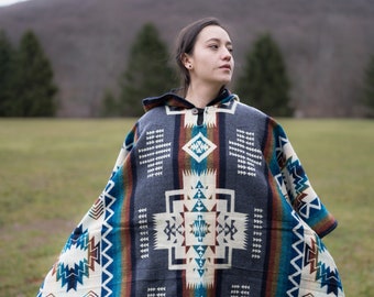 May include: A person wearing a blue, white, and brown patterned poncho with fringe. The poncho has a hood and a geometric design.