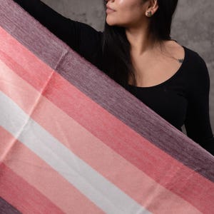 May include: A striped scarf in shades of pink, white, and purple. The scarf is held up, showing its design. The Paramo logo is visible in the bottom right corner.