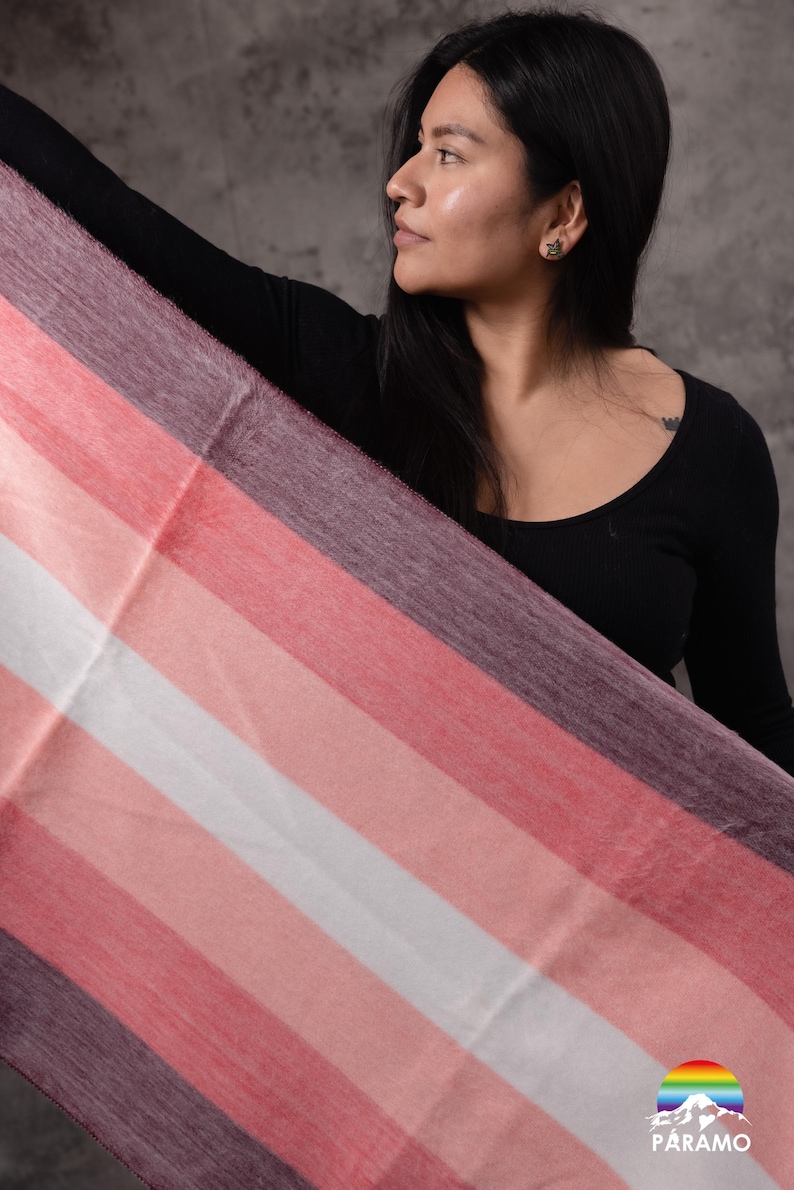 May include: A striped scarf in shades of pink, white, and purple. The scarf is held up, showing its design. The Paramo logo is visible in the bottom right corner.