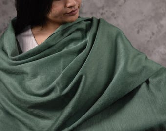 May include: A sage green shawl with a soft, textured appearance. The shawl is draped over the shoulders, with a fringed edge visible. The fabric has a subtle sheen, suggesting a luxurious material. The overall style is elegant and comfortable.
