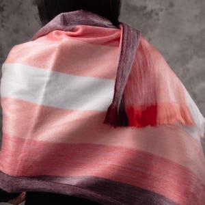 May include: A pink, white, and burgundy striped scarf with a fringed edge. The scarf is draped over the shoulders. The Paramo logo is visible in the bottom right corner.