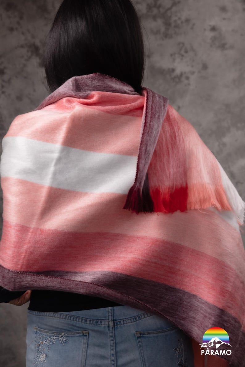 May include: A pink, white, and burgundy striped scarf with a fringed edge. The scarf is draped over the shoulders. The Paramo logo is visible in the bottom right corner.