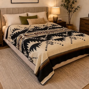 May include: A woven bed blanket featuring a geometric pattern in black, cream, and brown tones. The design includes repeating triangular and cross motifs across the center and edges, with horizontal stripes along the bottom border of the fabric.