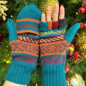 May include: Teal convertible fingerless gloves with a fold-over mitten cap. The gloves feature a multi-colored geometric pattern in orange, purple, and yellow, with a ribbed cuff. The mitten cap is secured over the fingers, showing a teal base color.