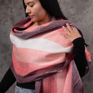 May include: A multi-coloured striped shawl in pink, white, and purple hues. The soft, fringed wrap is draped over the shoulders. The shawl is made of a soft, fuzzy material.