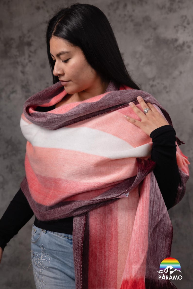 May include: A multi-coloured striped shawl in pink, white, and purple hues. The soft, fringed wrap is draped over the shoulders. The shawl is made of a soft, fuzzy material.