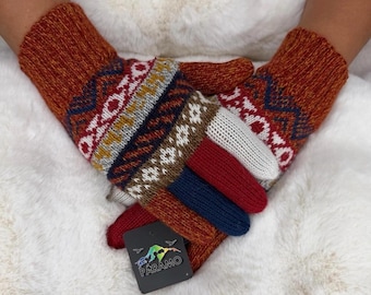 Op de afbeelding: Een paar gebreide handschoenen met een veelkleurig geometrisch patroon in tinten oranje, rood, blauw en wit. De handschoenen hebben een geribbelde boord en een zwart rechthoekig label met de tekst PARAMO en een bergafbeelding.
