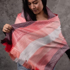 May include: A patterned scarf in red, pink, white, and purple stripes, with a fringed edge. The scarf is draped over the shoulders. The Paramo logo is visible in the bottom right corner. The scarf is a stylish accessory.