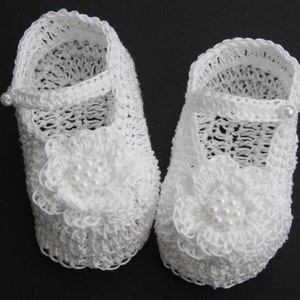 Peut inclure: Une paire de chaussons de b&eacute;b&eacute; blancs, crochet&eacute;s. Chaque chaussure est orn&eacute;e d'une bride avec un bouton perl&eacute; et d'une fleur d&eacute;corative avec des perles sur le bout. Les chaussures sont con&ccedil;ues avec un motif ajour&eacute;.