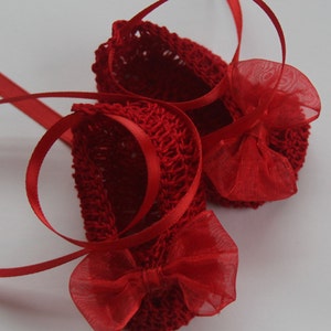 K&ouml;nnte beinhalten: Ein Paar kleine, rote geh&auml;kelte Babyschuhe mit zarten Schleifen und Satinb&auml;ndern. Die Schuhe sind leuchtend rot und haben ein strukturiertes Strickmuster. Die Schleifen sind aus einem transparenten, roten Stoff gefertigt.