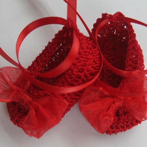 K&ouml;nnte beinhalten: Ein Paar handgefertigte rote Baby-H&auml;kel-Booties mit roten B&auml;ndern und Schleifen aus Chiffon. Die Booties sind aus einem strukturierten Garn gefertigt und f&uuml;r Babys konzipiert.
