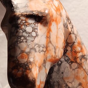 Puede incluir: Escultura de cabeza de caballo de m&aacute;rmol con un dedal plateado en la cabeza. La escultura presenta un patr&oacute;n de remolinos naranjas, blancos y negros. El dedal es plateado con una banda decorativa.