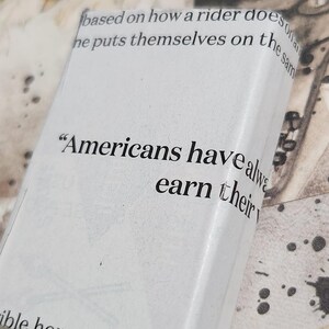 May include: A white rectangular object with text that reads "Americans have always earn their". The object is on a background with text and ink splatters. The text is partially visible.