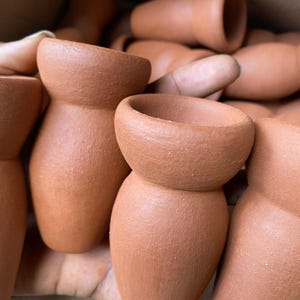 Puede incluir: Primer plano de varios cuencos de arcilla de terracota. Los cuencos son sin esmaltar y tienen una superficie rugosa y texturizada. Los cuencos están apilados uno encima del otro.