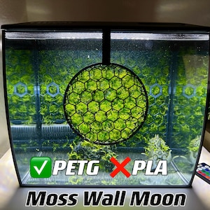 Op de afbeelding: Een zwart aquarium met een heldergroene moswand maan decoratie. Het mos zit in een zwart, honingraatvormig frame. De tekst "Moss Wall Moon" staat onderaan, samen met de labels "PETG" en "PLA".