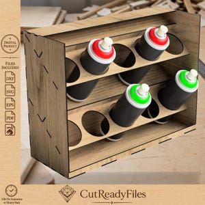 Puede incluir: Un organizador de madera para botes de pintura en aerosol con seis botes. Los botes son negros con tapas rojas y verdes. El organizador es de madera clara y tiene forma rectangular con aberturas circulares.