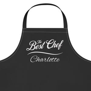 以下が含まれることがあります： 黒いエプロン。首に掛けるループとウエストの紐が付いています。「The Best Chef」の文字が筆記体で書かれ、その下に「Charlotte」という名前があります。キッチンでの使用を目的としています。