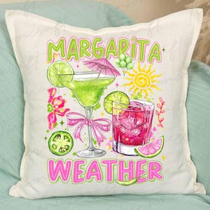 May include: Off-white square pillow with a colorful margarita design. The design features two cocktails, lime slices, a sun, and the words "Margarita Weather" in green and pink. A fun, decorative pillow.