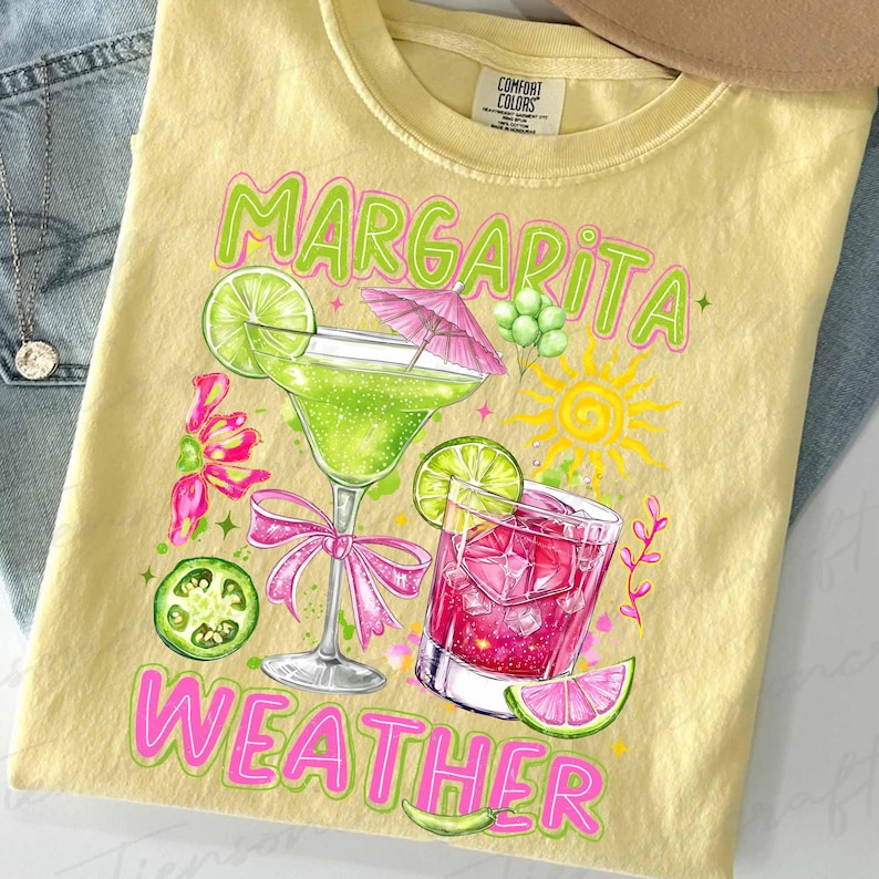 May include: Yellow t-shirt with a colorful graphic of two cocktails, a margarita and a pink drink, with lime slices and a sun. The words "Margarita Weather" are printed in green and pink.