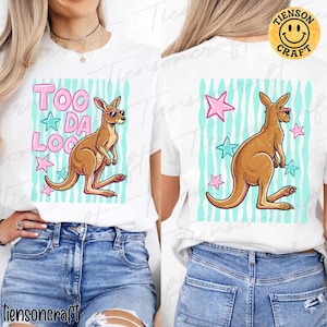 May include: White t-shirt with a cartoon kangaroo wearing sunglasses. The front design features the text "TOO DA LOO" in pink, with stars and a blue striped background. The back of the shirt has a similar kangaroo design with stars.