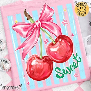 May include: Pink t-shirt featuring a vibrant illustration of two cherries tied with a pink bow. The design includes blue vertical stripes, the word "Sweet" in green, and small floral and star accents. The shirt has the text "Better Craft" and a smiley face logo.