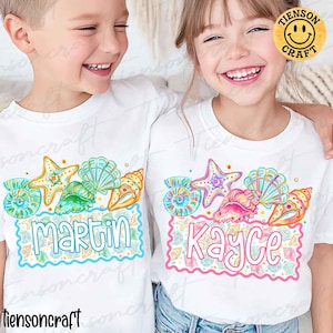 May include: White t-shirts with a colorful seashell design and personalized names. The design includes starfish, seashells, and the names "Martin" and "Kayce" in a playful font. The shirts are perfect for a beach or summer theme.