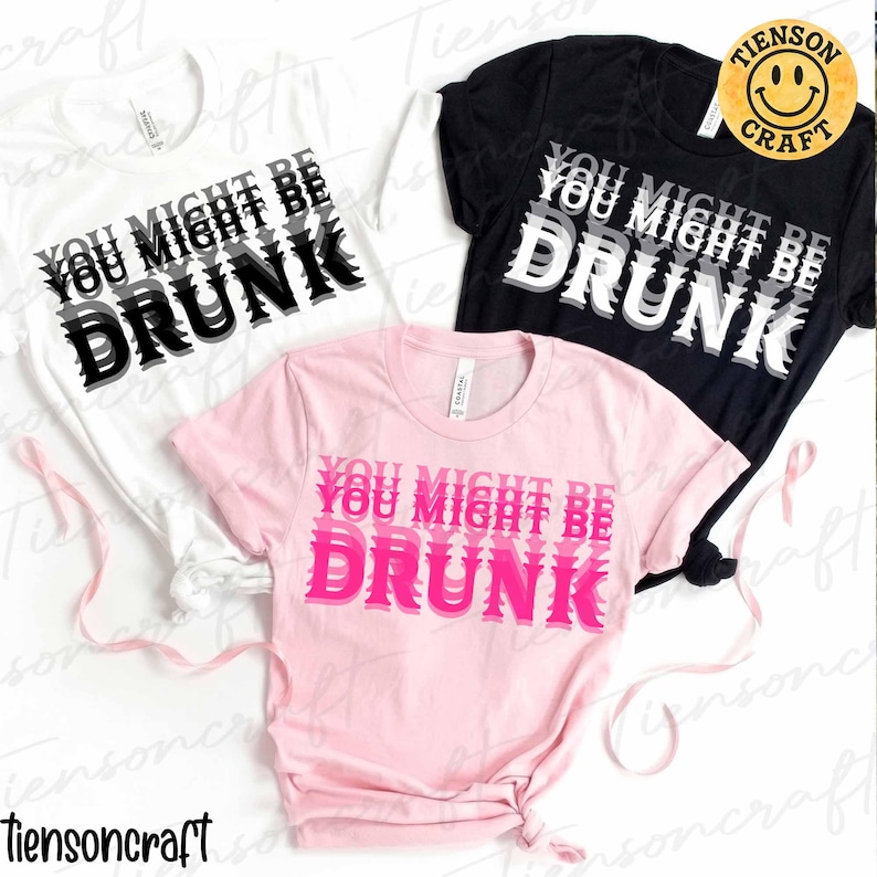 May include: Three t-shirts, white, black, and pink, each displaying the text "YOU MIGHT BE DRUNK" in a layered, bold font. The white and black shirts have black and white text, while the pink shirt has pink text.