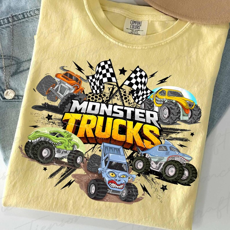 May include: Pale yellow t-shirt with a vibrant graphic of monster trucks. The design showcases several monster truck illustrations, chequered flags, and the text "MONSTER TRUCKS" in bold, orange and yellow letters.
