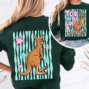 May include: Dark green sweatshirt with a kangaroo wearing sunglasses, set against a backdrop of blue and white stripes and pink and blue stars. The text "TOO DA LOO" is also visible.