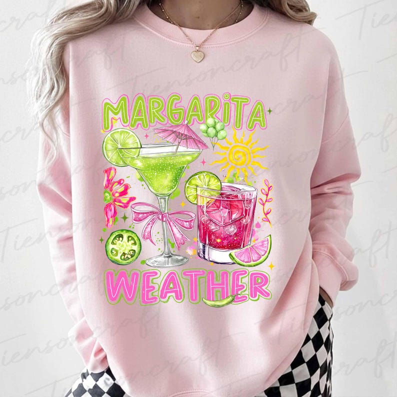 May include: Pink sweatshirt with a colorful graphic of two cocktails, lime slices, and the words "Margarita Weather" in green and pink. The design includes a margarita glass with a pink bow and a drink with ice cubes.