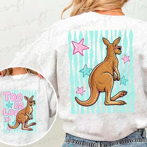 May include: A light grey sweatshirt with a kangaroo wearing sunglasses, set against a backdrop of blue stripes and pink and blue stars. The text "TOO DA LOO" is also displayed on the sweatshirt.