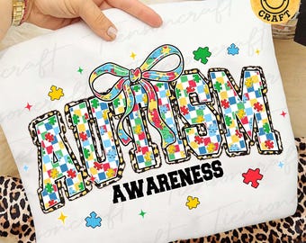 May include: White sweatshirt with the word "AUTISM" in large, colorful puzzle piece letters, and a matching bow. The word "AWARENESS" is printed below in black. Scattered puzzle pieces and stars decorate the design.