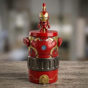 May include: A cylindrical red and gold beverage container featuring a molded Iron Man armor design on the exterior. A small Iron Man figurine is attached to the top lid, which includes a straw. The base has a dark metallic band and a gold spout.