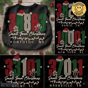 May include: A black sweatshirt featuring a graphic with the text Small Town Christmas, a string of colorful holiday lights, a gingerbread man, a snowman, and a Santa hat. The design includes large numbers and location names like Pontotoc, MS.
