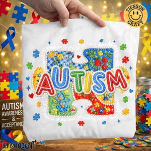 May include: White tote bag with the word "AUTISM" in colorful, embroidered puzzle piece letters. The bag features floral and patterned designs within the puzzle pieces and scattered puzzle piece accents. The words "Autism Awareness & Acceptance" are on a wooden block.