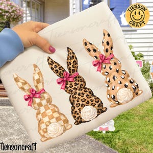May include: Three decorative Easter bunny figures with pink bows and white rosebud tails. The bunnies have different patterns: checkered, leopard print, and spotted. The image has the text "Tiensoncraft".